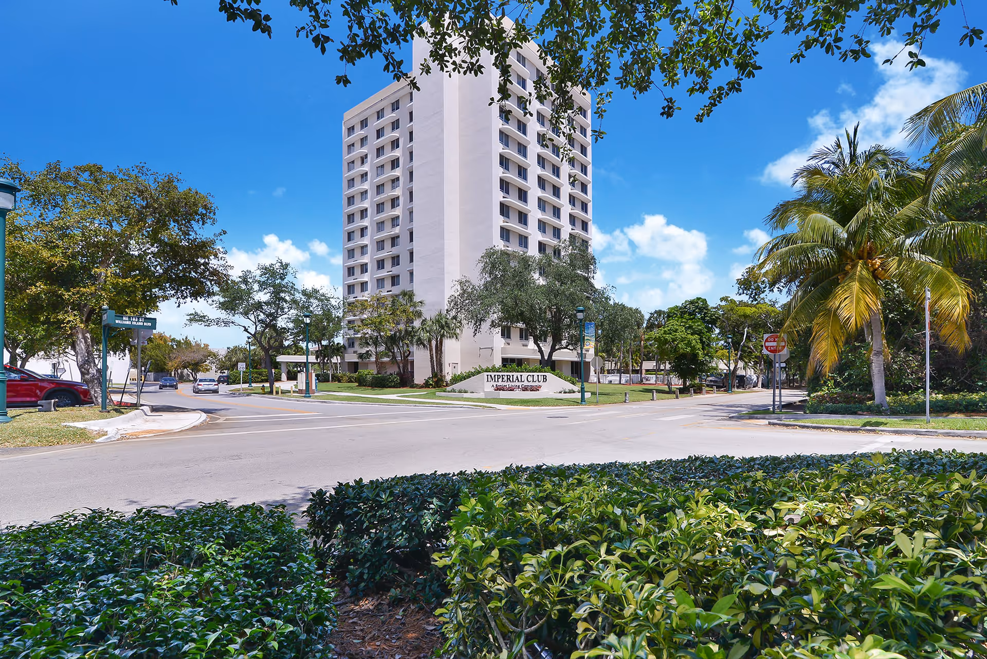 High-rise Imperial Club senior living building viewed across the street with palm trees and landscaped greenery.