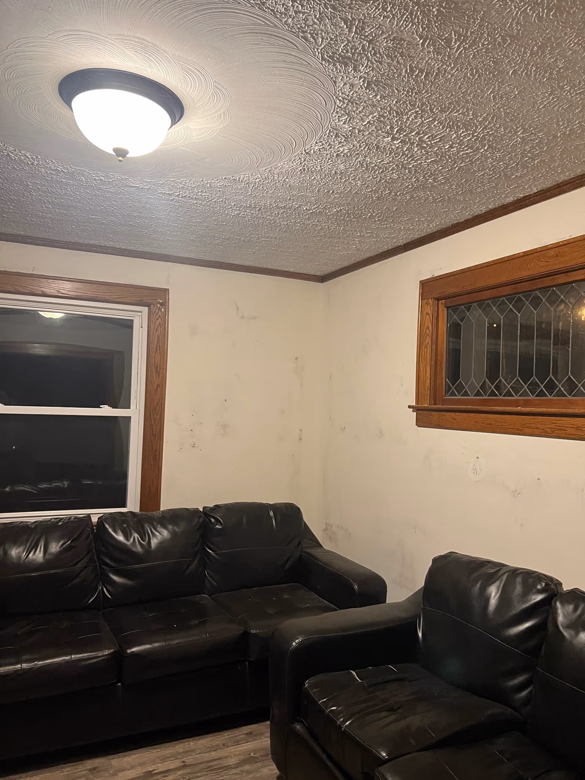 Living room with black leather sofas, stained walls, wooden trim, and a ceiling light.