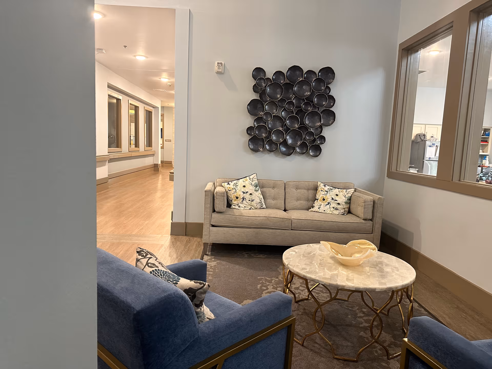 A cozy lobby seating area with beige sofa, blue chair, marble coffee table, and wall sculpture.
