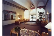 Spacious senior living room with sofas, lamps, plants, and a glass door entrance.