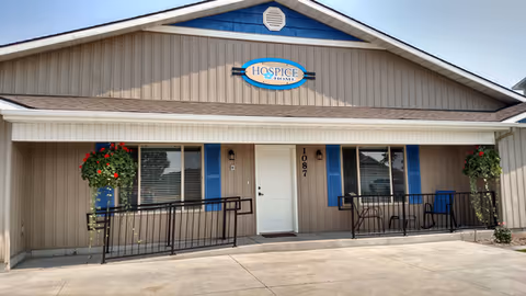 Front exterior of Hospice of Eastern Idaho, beige siding, blue doors, hanging flower baskets.
