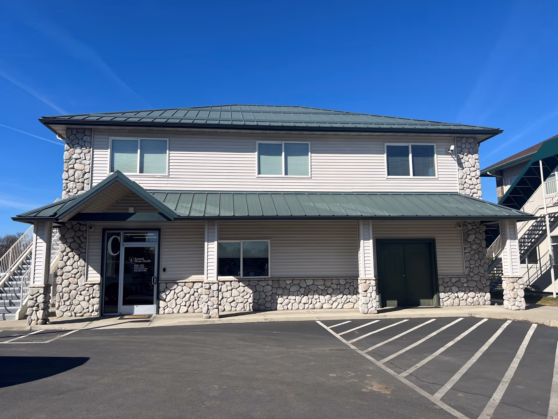 Assured Home Health facility exterior: two-story building with stone accents and a green metal roof.