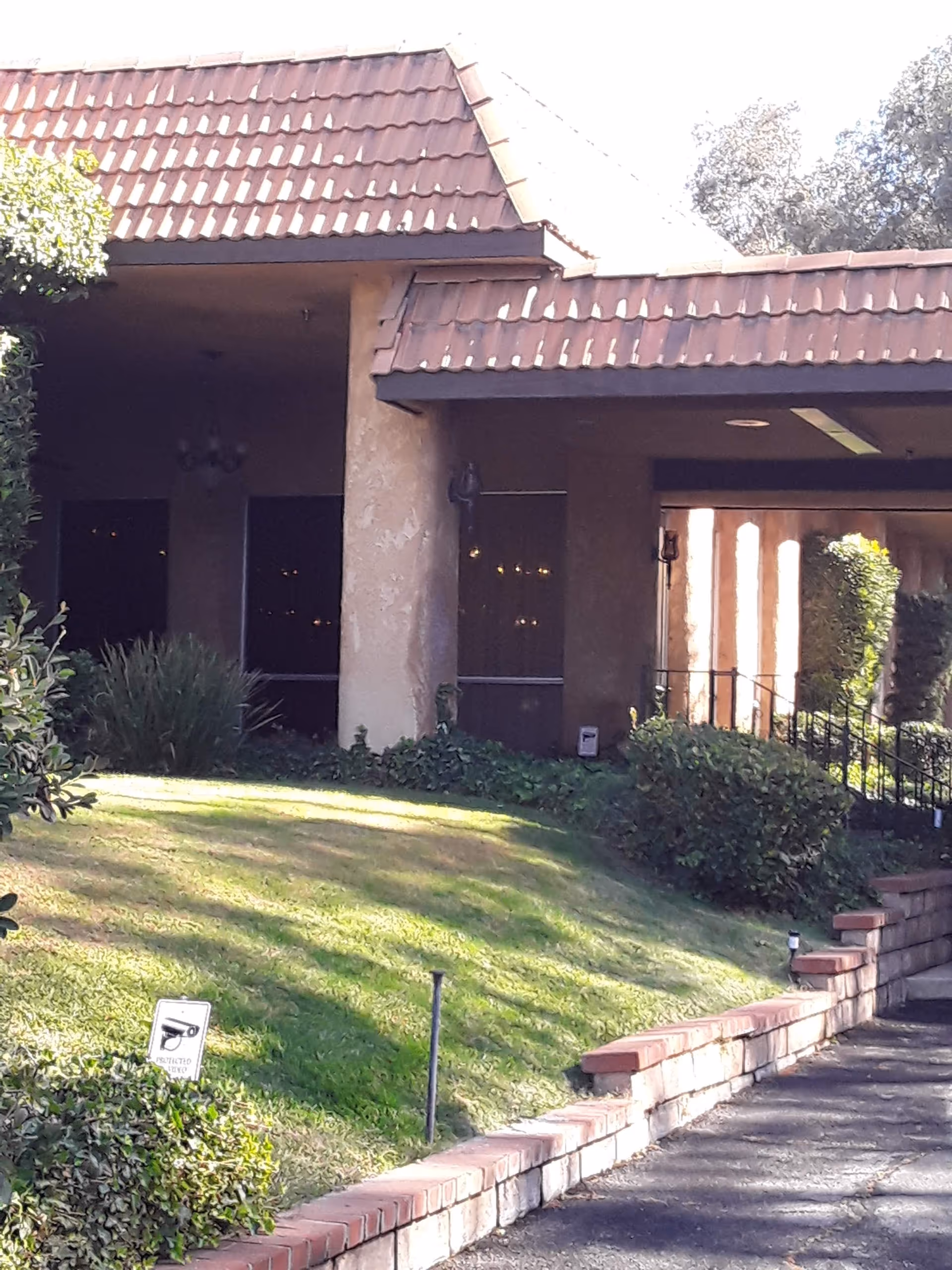 Exterior view of a Mediterranean-style senior living facility with tiled roof and lawn.