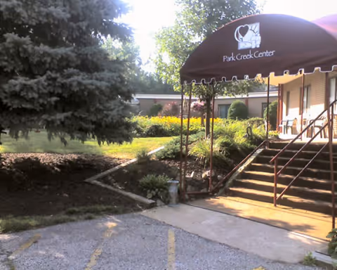 Entrance to Park Creek Center showing a maroon awning over outdoor steps, handrails, and landscaped grounds.