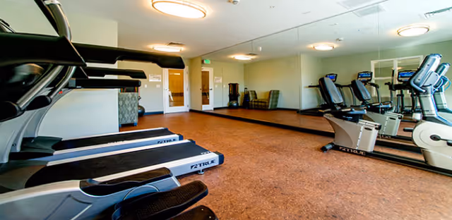 Indoor fitness room with treadmills, stationary bikes, mirrors, and warm-toned flooring.