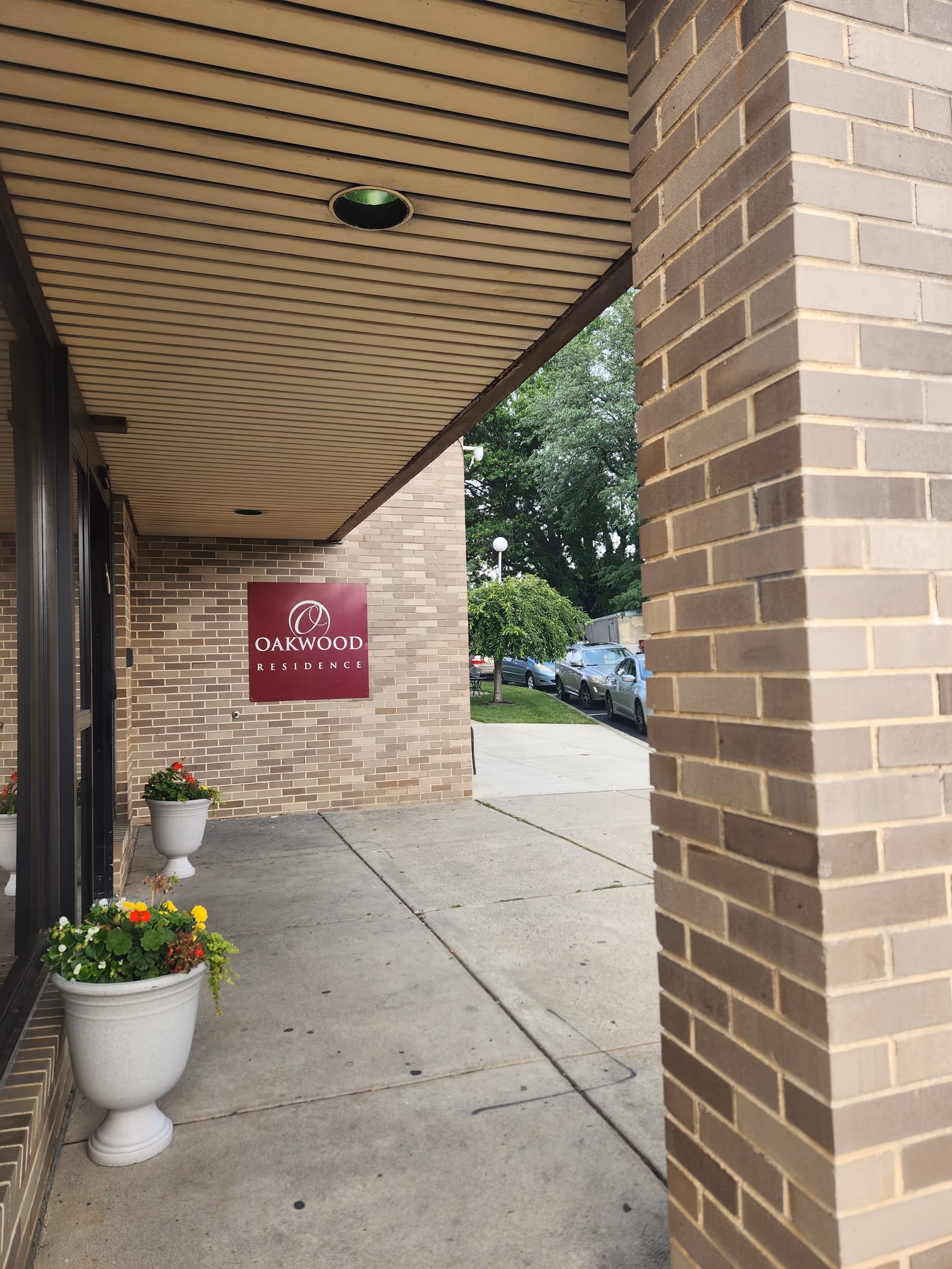 Exterior view of Oakwood Residence with sign, planters, and parked cars.
