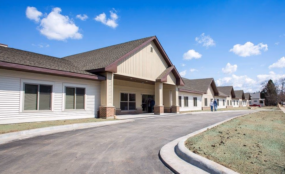 Row of beige, single-story senior living buildings with a curved driveway.