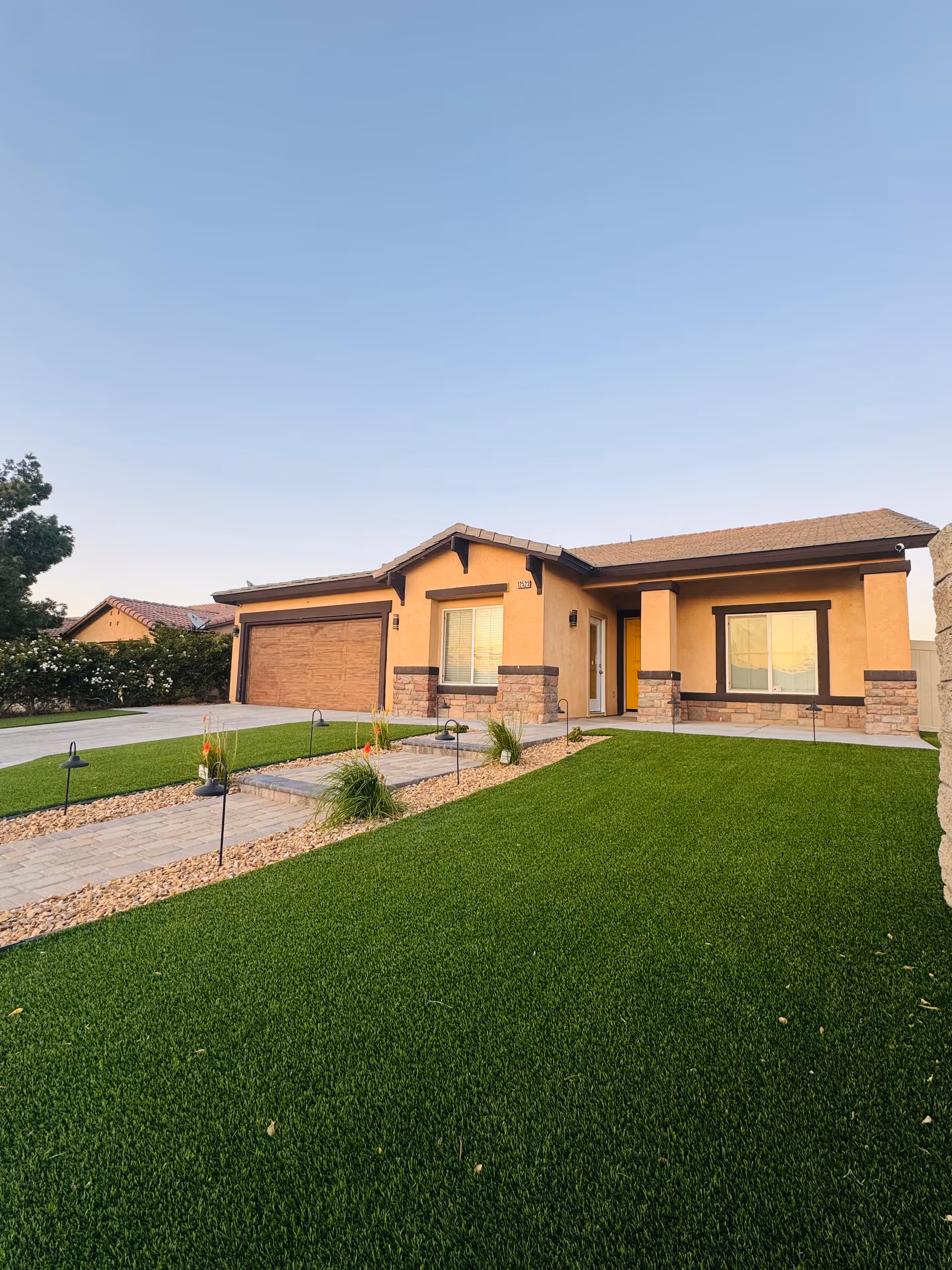 Front exterior of a single-story tan residential home with a manicured lawn and driveway.