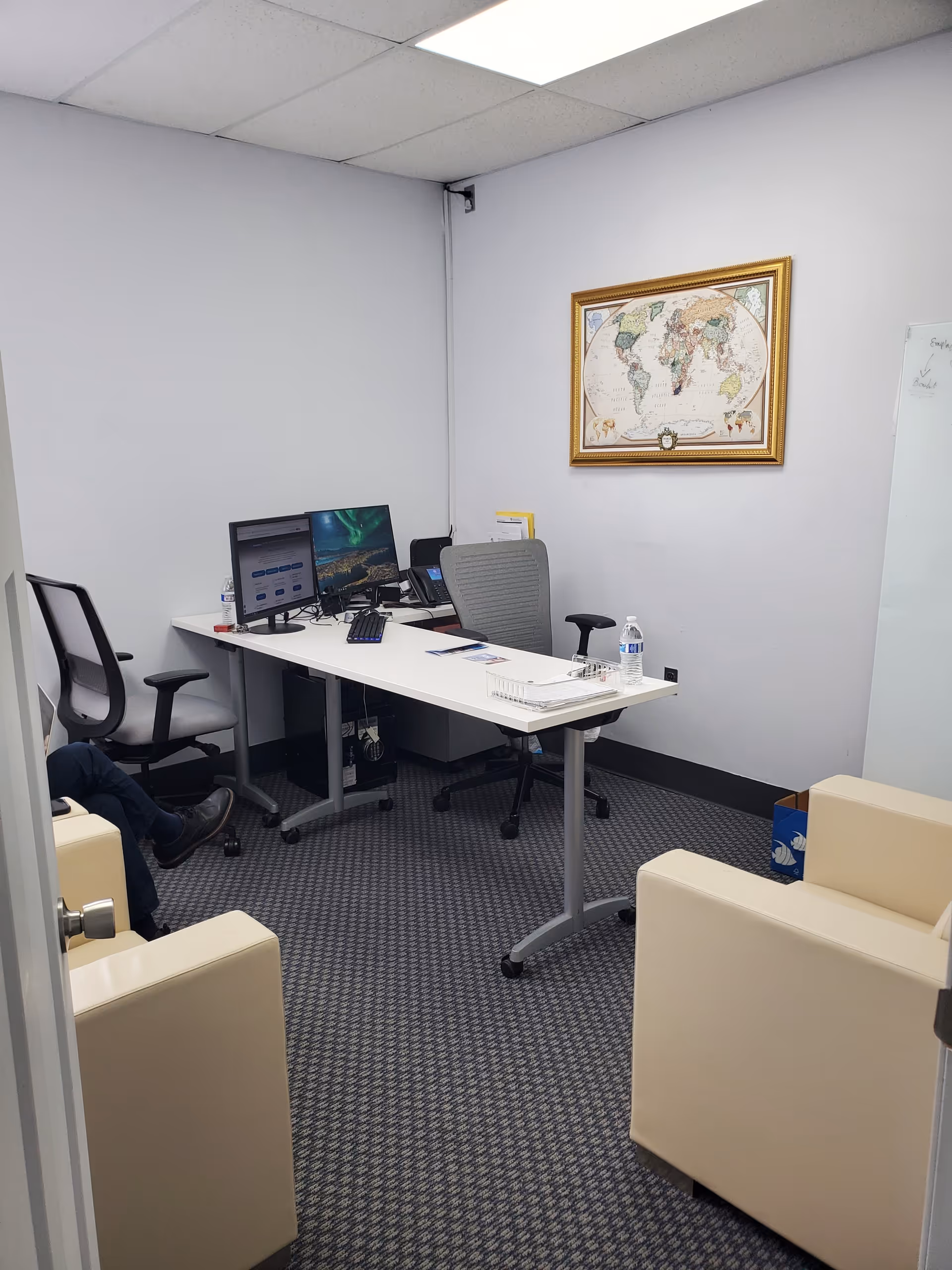 Small office with desks, computers, a world map on the wall, and beige seating.
