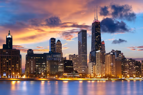 Sunset over a city skyline reflected on calm water.