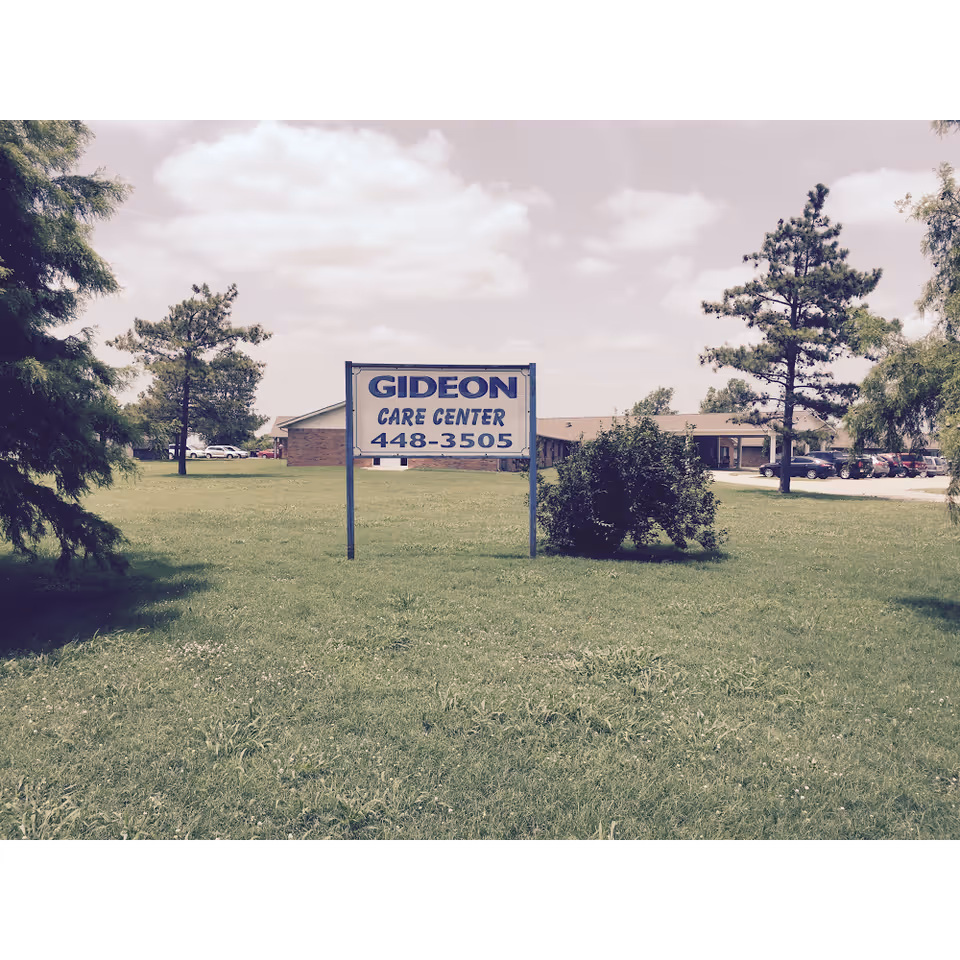 A Gideon Care Center sign sits on a grassy lawn with a building and trees.