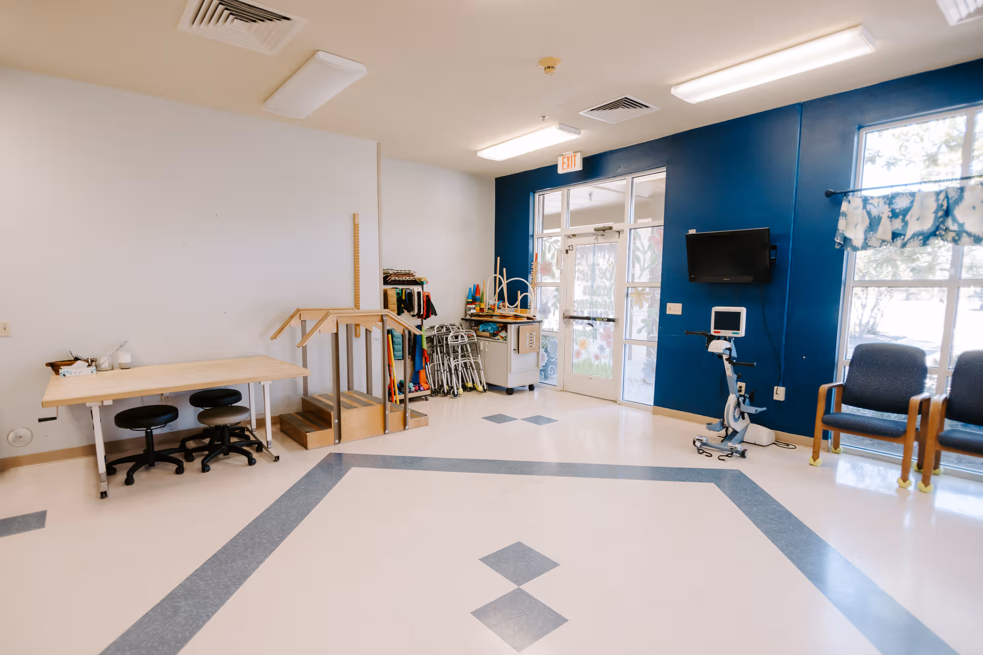 Therapy room with blue accent wall, exercise equipment, a TV, and seating.