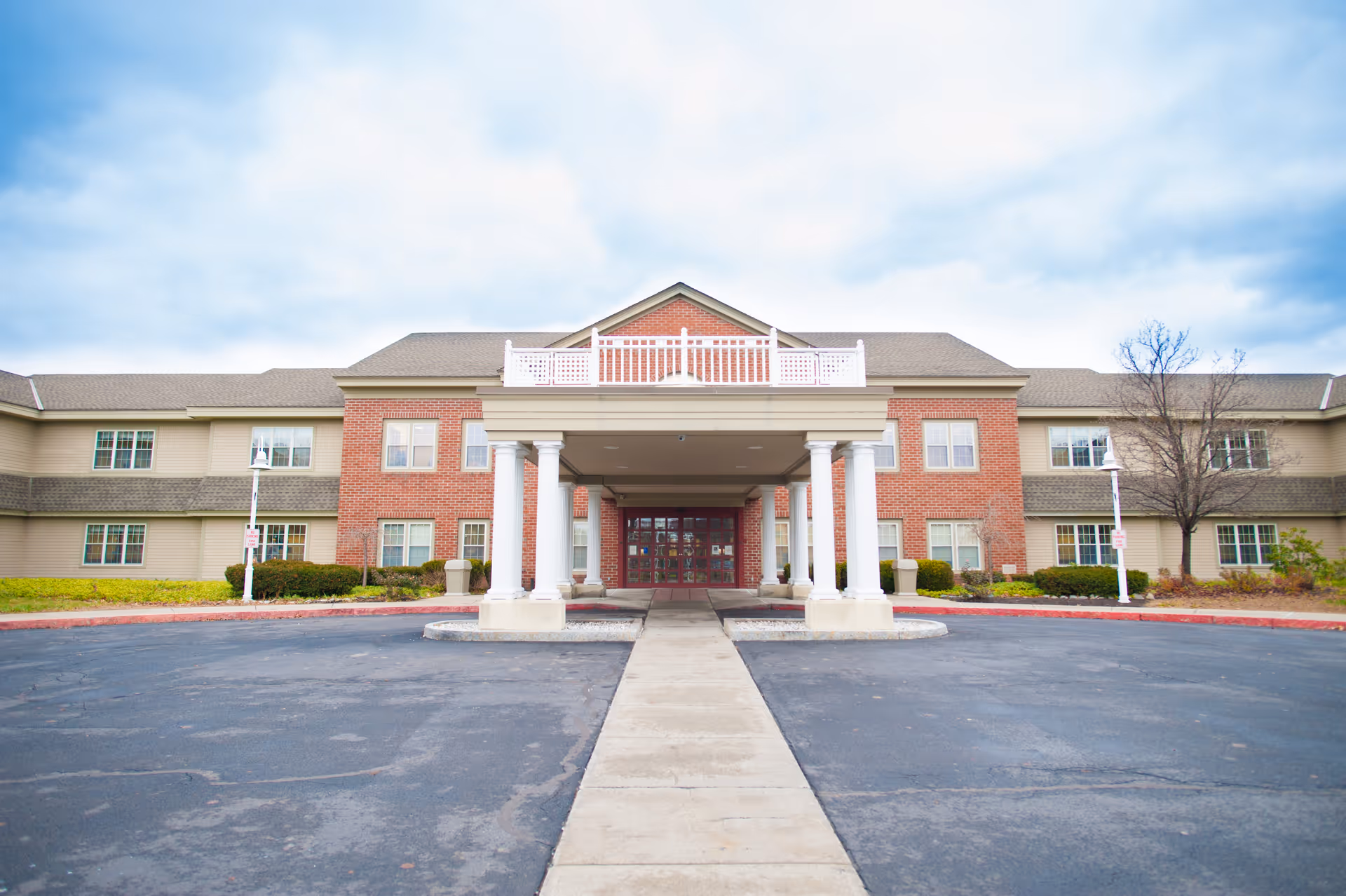 Front exterior view of EverGreen Commons Rehabilitation and Nursing Center, showing a two-story building with a covered entrance supported by white columns, brick and beige siding, and a paved driveway leading up to the entrance.