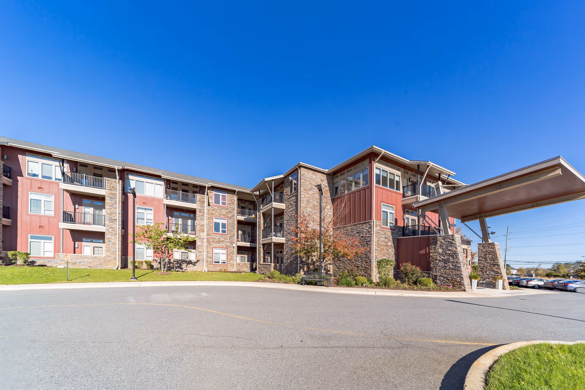 Sunny exterior view of a senior living facility with stone accents and a covered entrance.