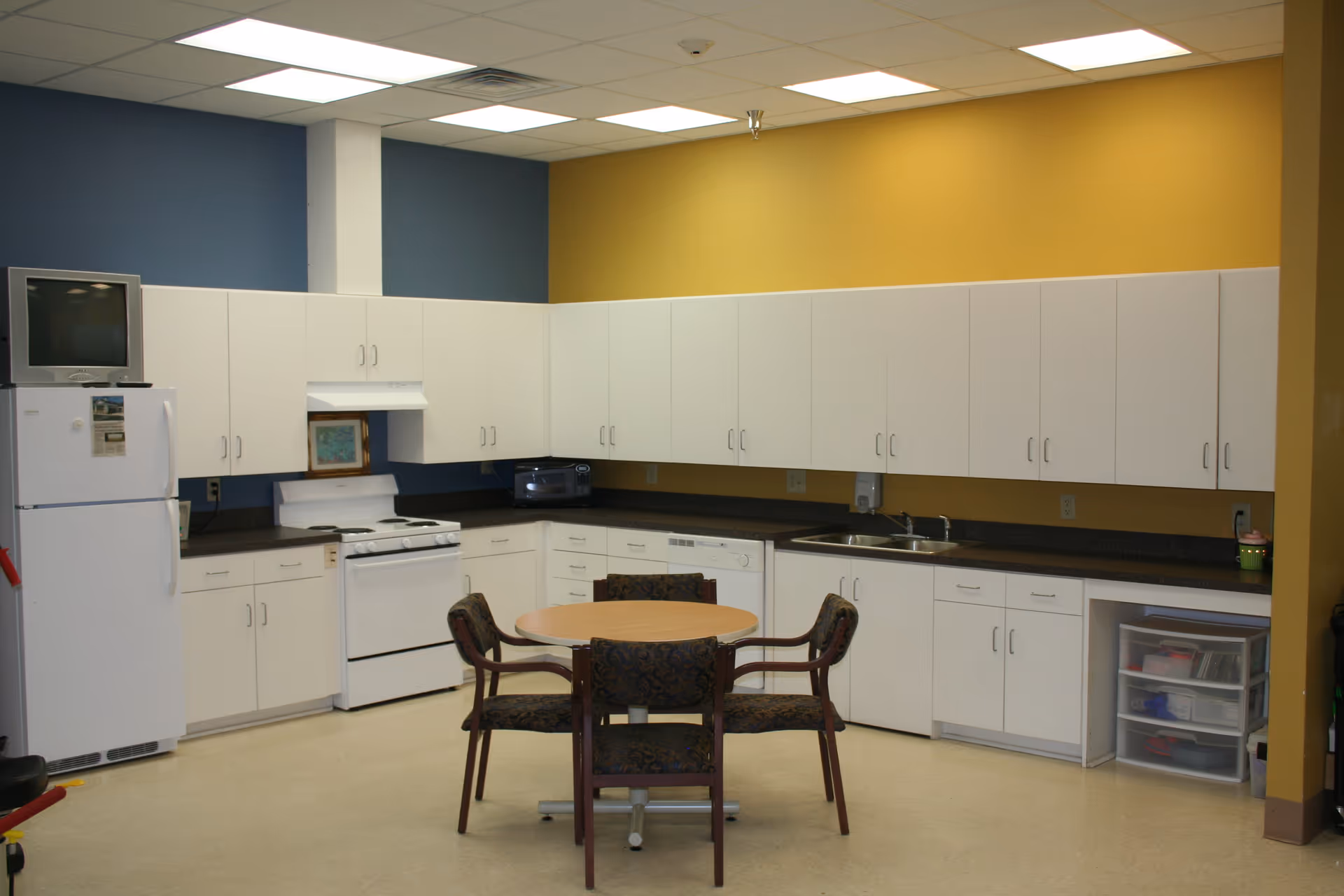 White kitchen with cabinets, stove, refrigerator, and a round table with chairs.