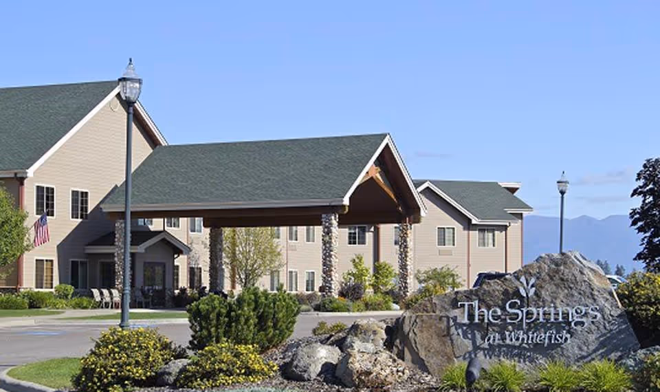 Exterior view of The Springs at Whitefish entrance with sign, shrubs, and porte-cochere.