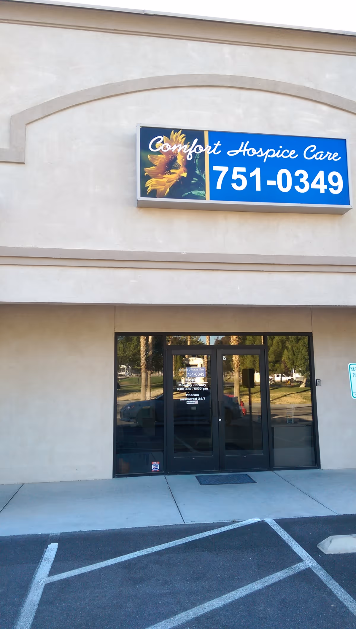 Front exterior of Comfort Hospice Care building with blue sign and glass doors.