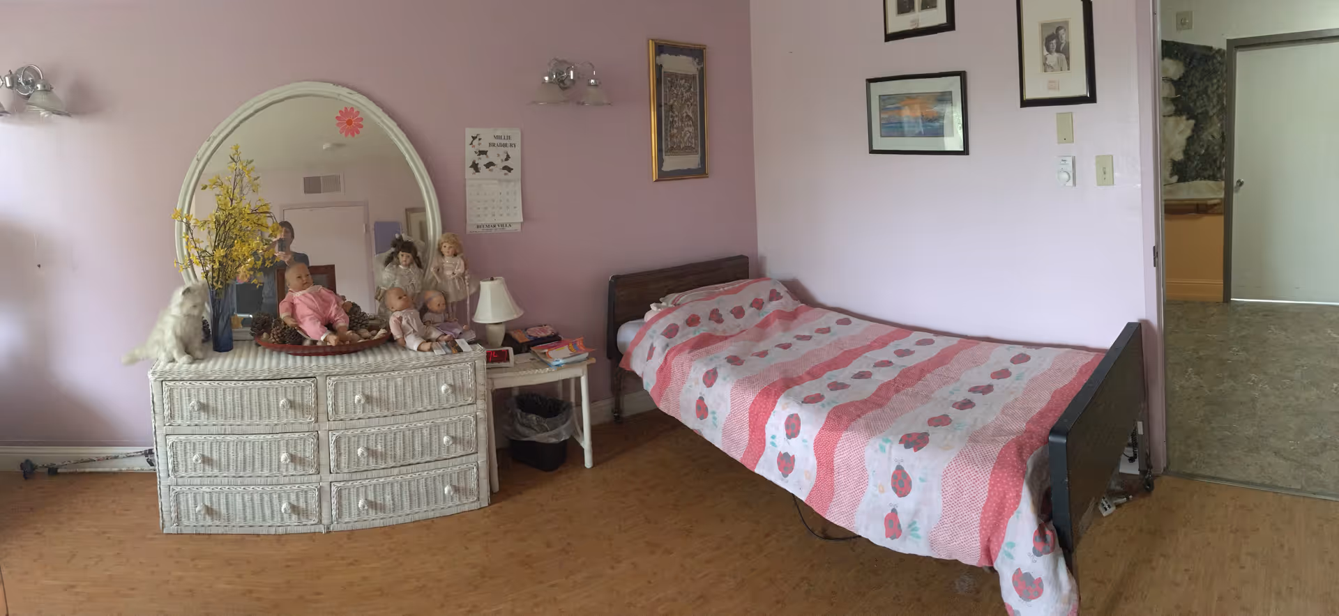A pink-walled bedroom featuring a striped pink bed, large dresser with mirror, and dolls.