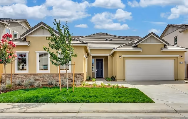 Single-story beige residential building with a front yard, driveway, and a blue door beside a garage.