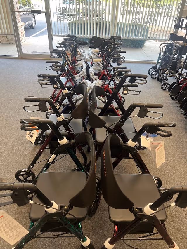 Multiple walkers and rollators lined up inside a bright showroom near glass doors.