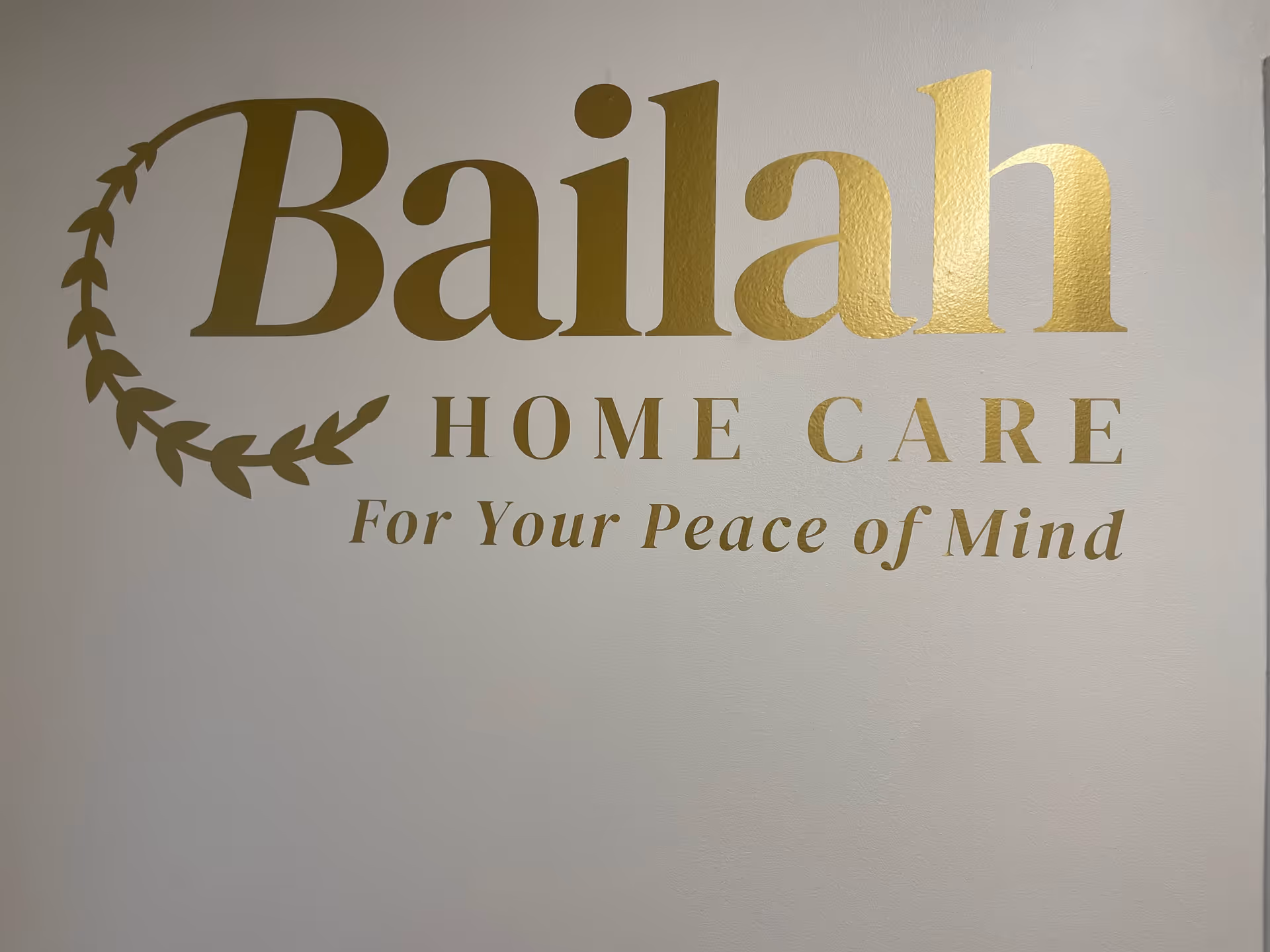 Gold Bailah Home Care sign on a plain light interior wall.