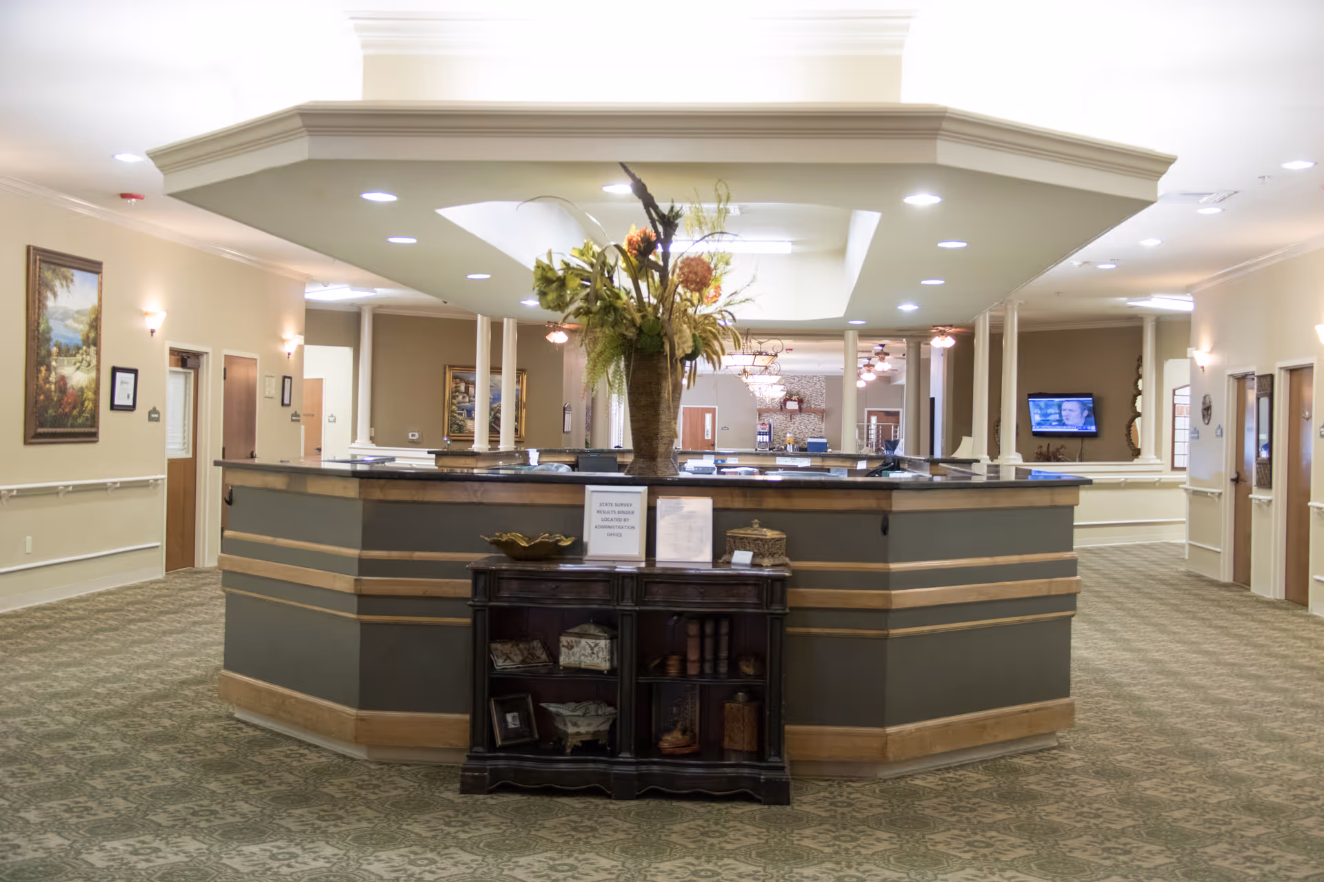 Circular reception desk in a well-lit senior living lobby with a large flower arrangement.