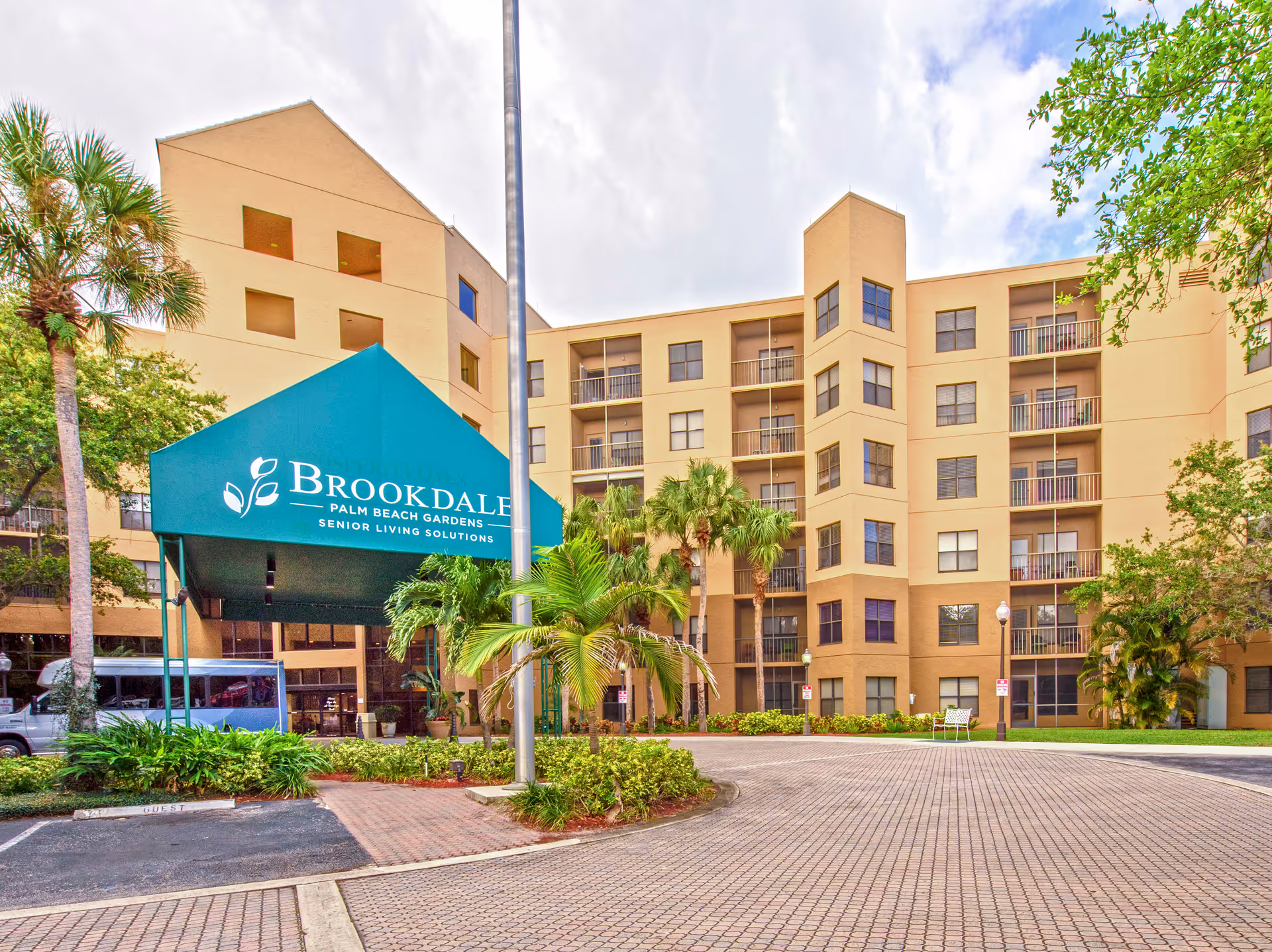 Exterior view of Brookdale Palm Beach Gardens entrance with a teal canopy and palm trees.