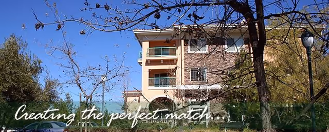 Exterior view of a senior living building with trees and blue sky.