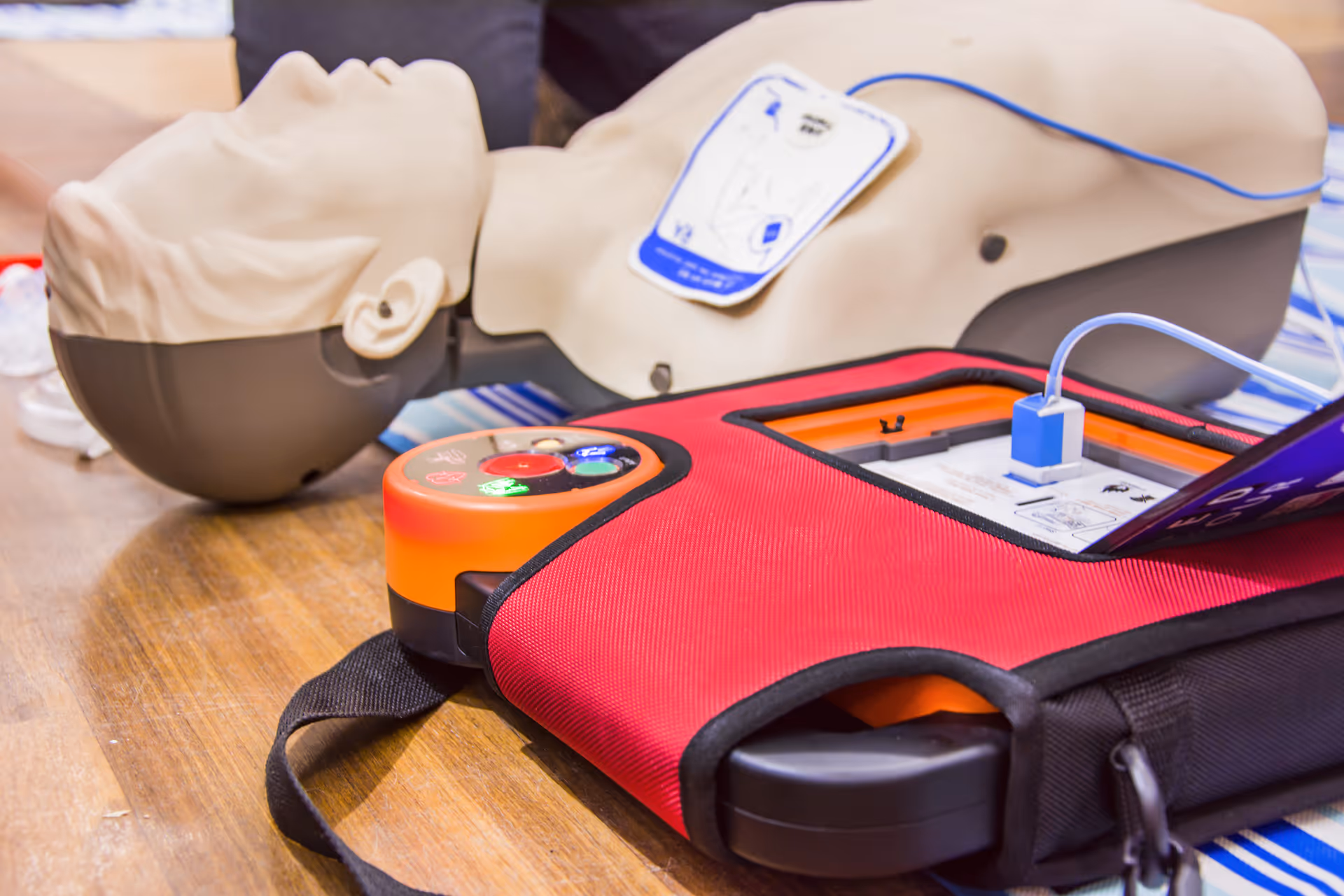 Close-up of a CPR manikin and a defibrillator training device on a wooden table indoors.