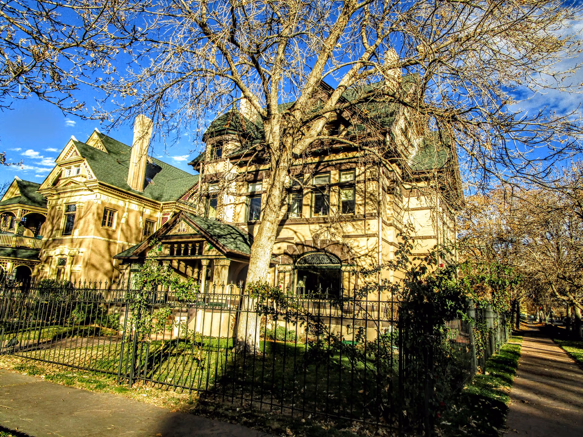Ornate Victorian-style senior living facility exterior with trees, a wrought-iron fence, and a sidewalk.