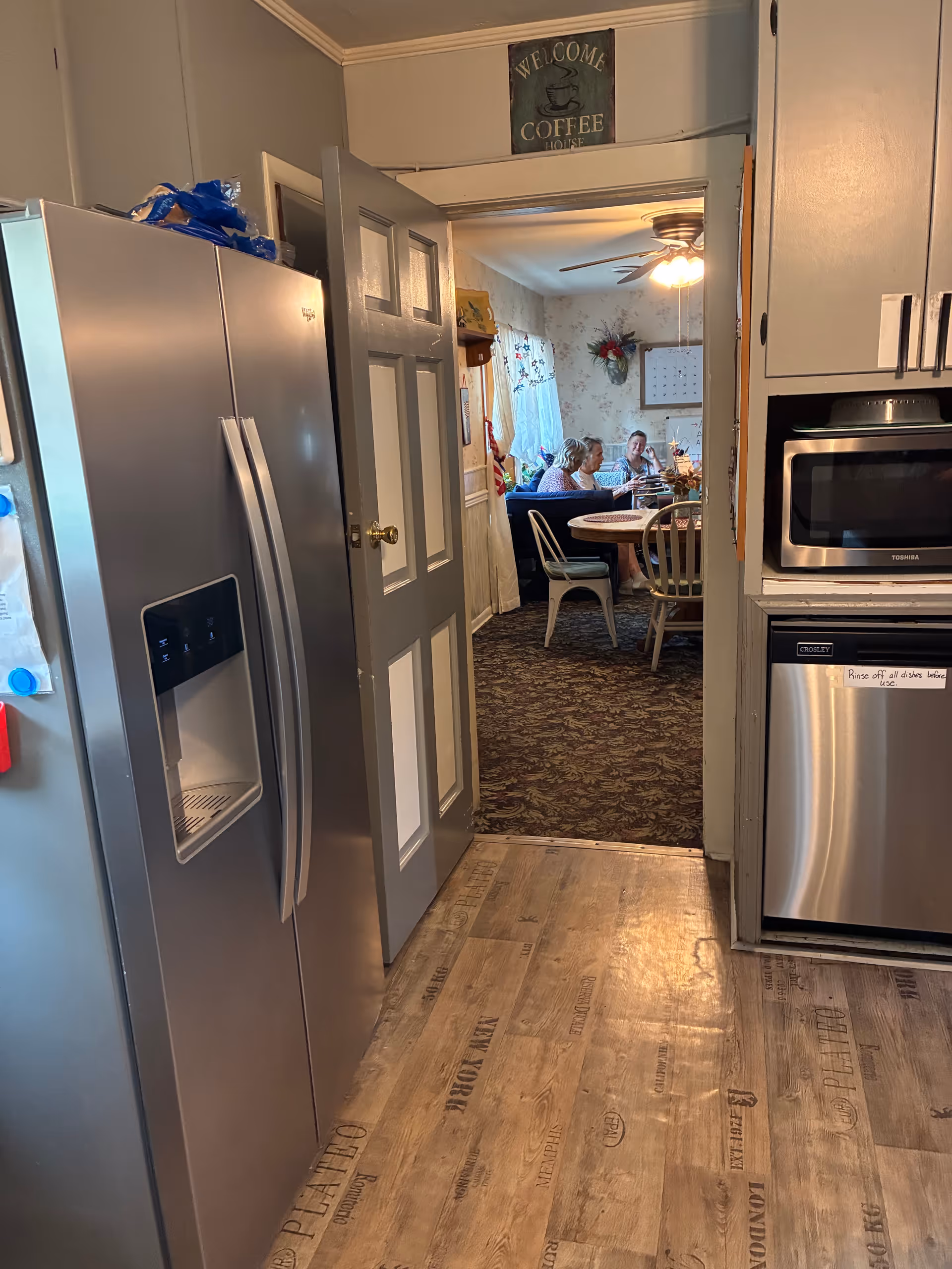 Modern kitchen leads to a dining area where residents are seated at a table.
