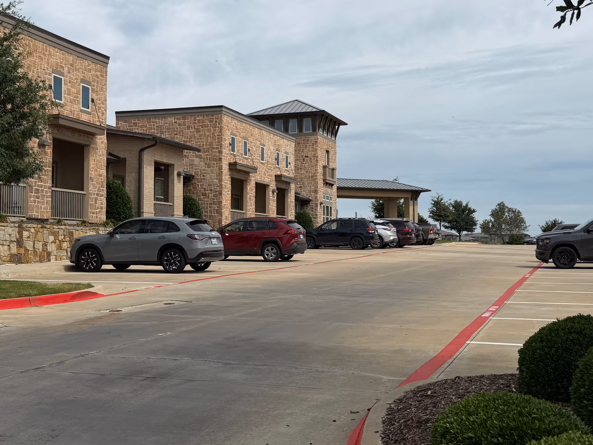 Stone-clad senior living facility with parked cars along a wide driveway.