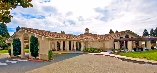 Senior living facility exterior with stucco walls, red tile roof, and arched entrance.