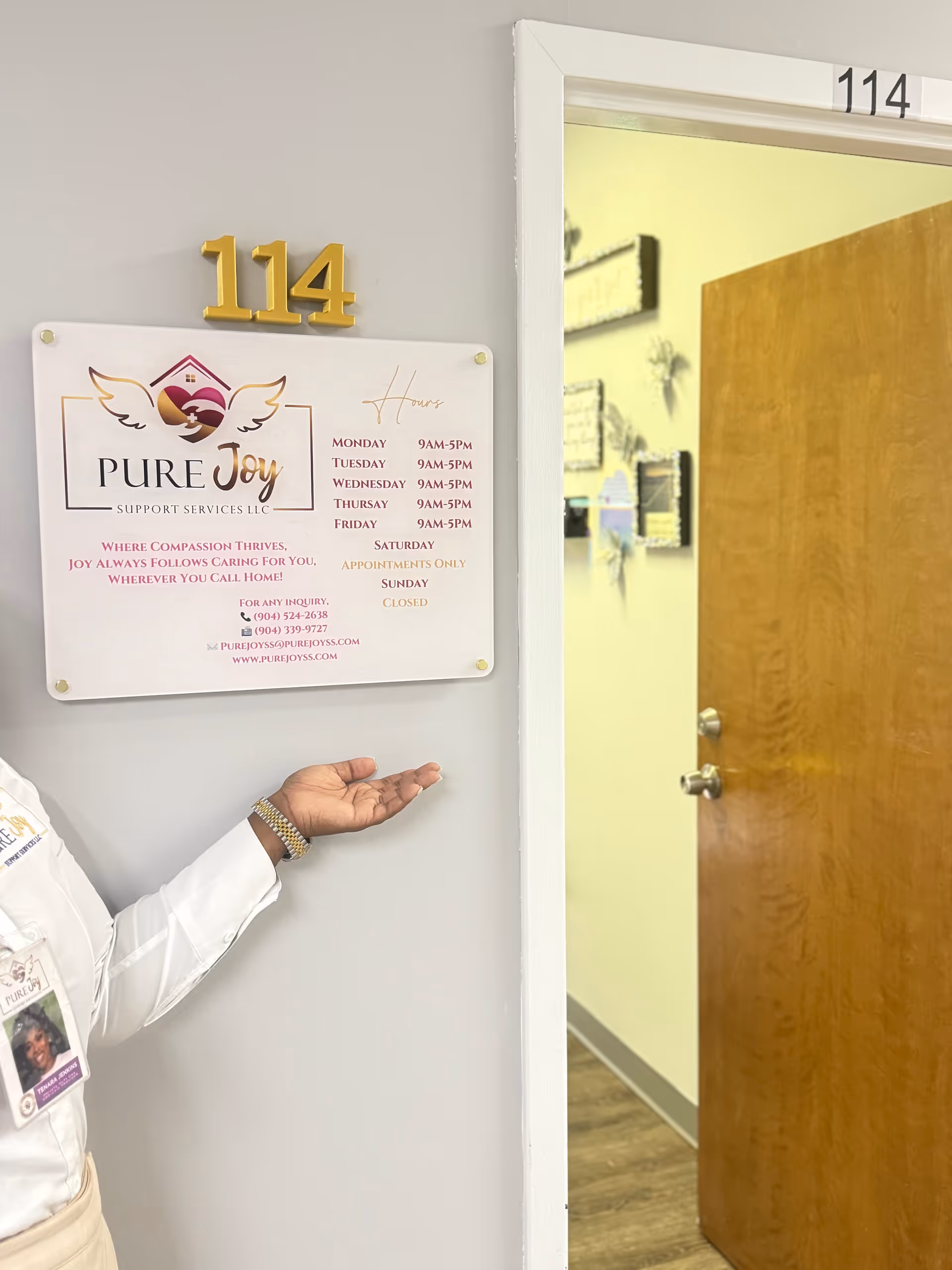 Interior hallway with door 114 and a staff member presenting a Pure Joy sign.