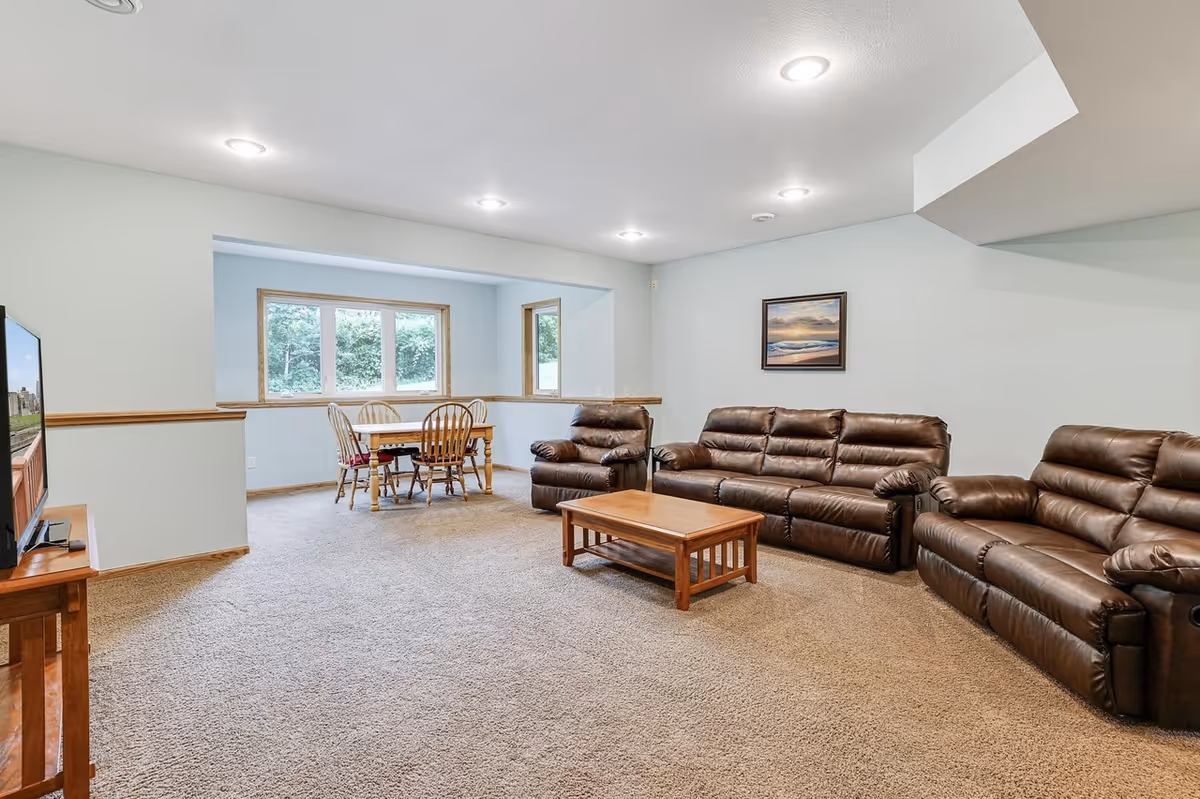 Bright communal living area with brown leather sofas, coffee table, and a dining nook near windows.
