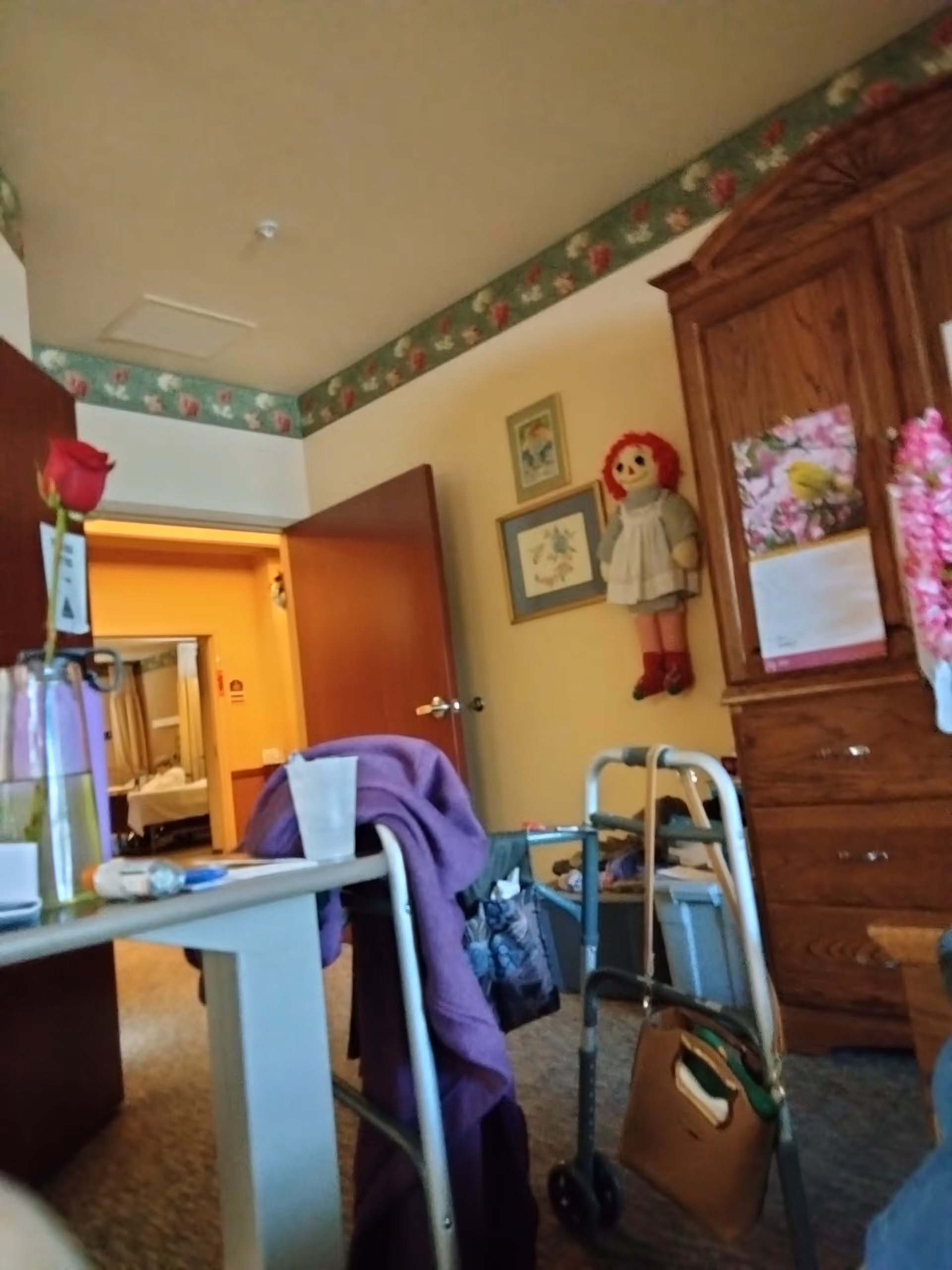 Interior view of a senior living room with a walker, table, and wooden cabinet.