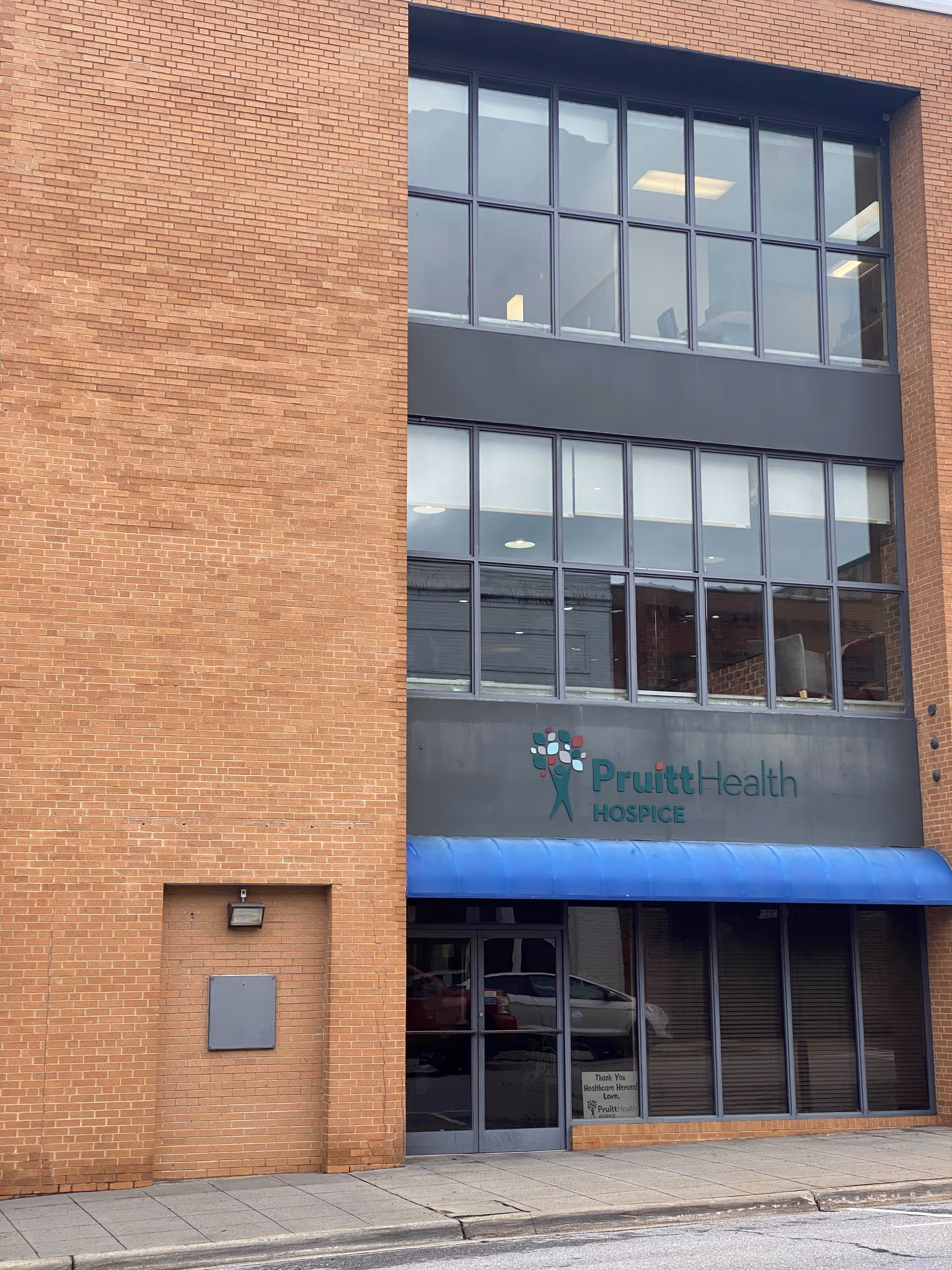 Brick building facade with large windows and blue awning at hospice entrance.