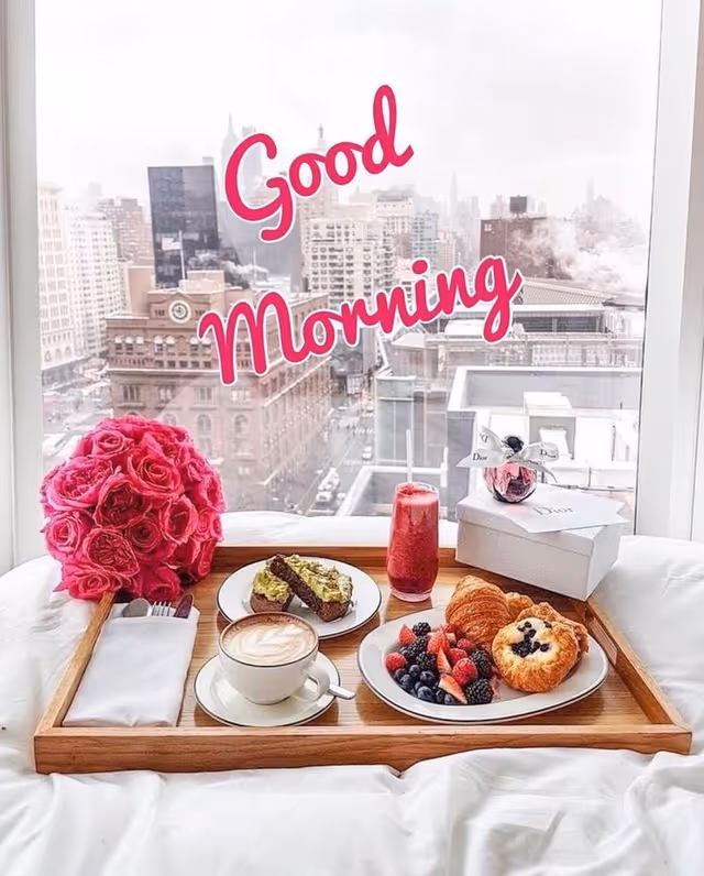 Breakfast tray on a bed with coffee, pastries, berries, and a pink bouquet.