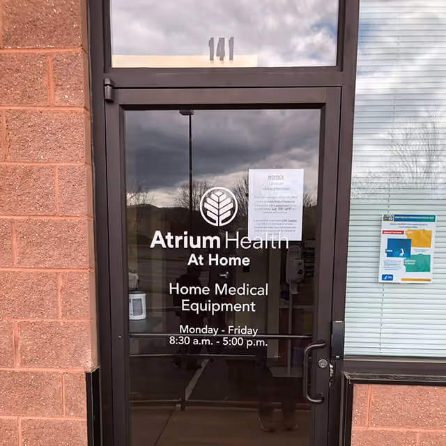 Glass entrance door displaying Atrium Health At Home signage on brick exterior