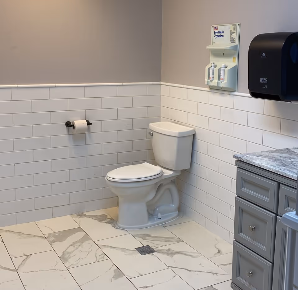 Clean, modern care center bathroom with toilet, tiled walls, and gray cabinet