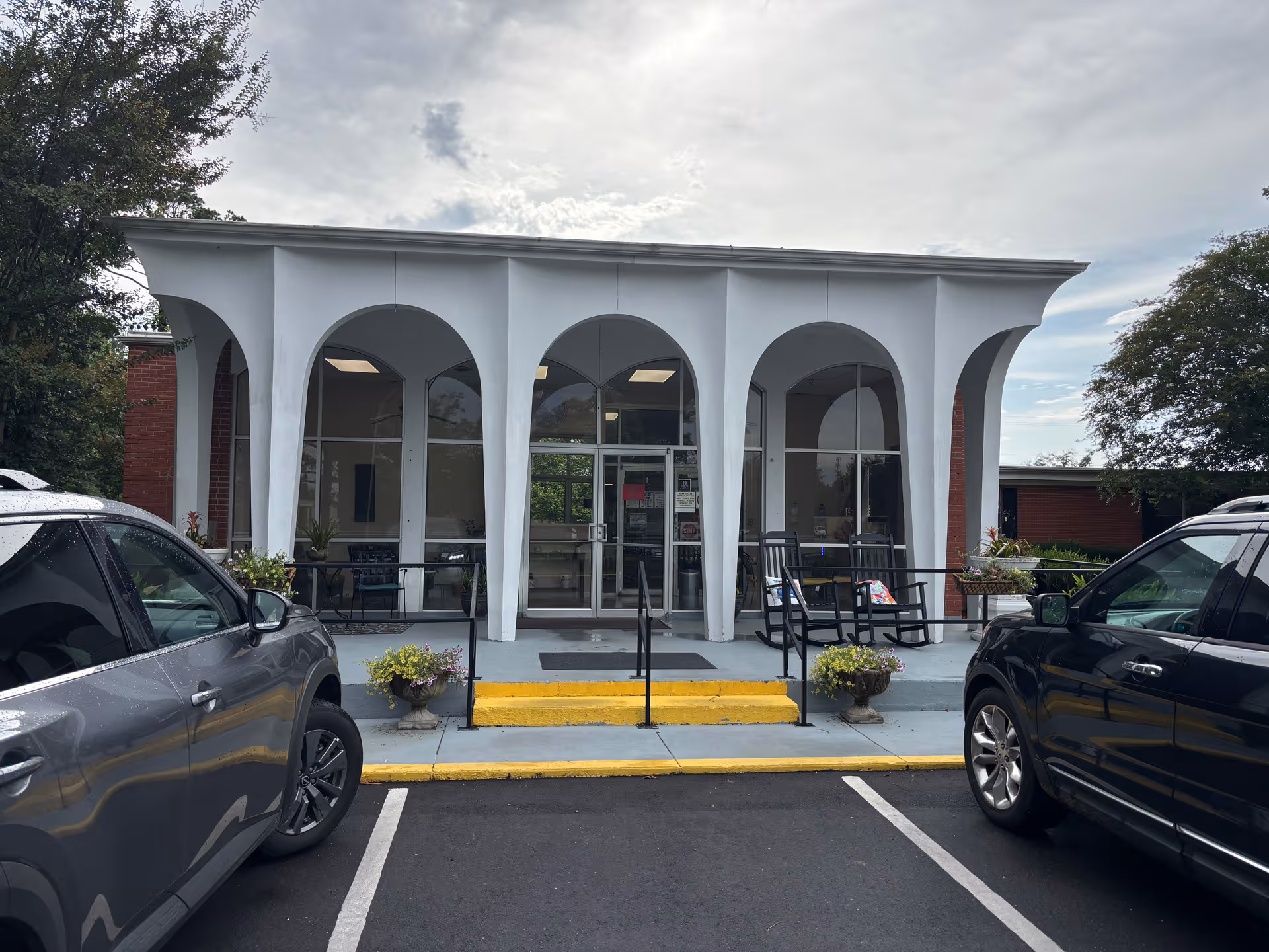 Front entrance of Glen Oaks Nursing Center with arched white columns and parked cars.
