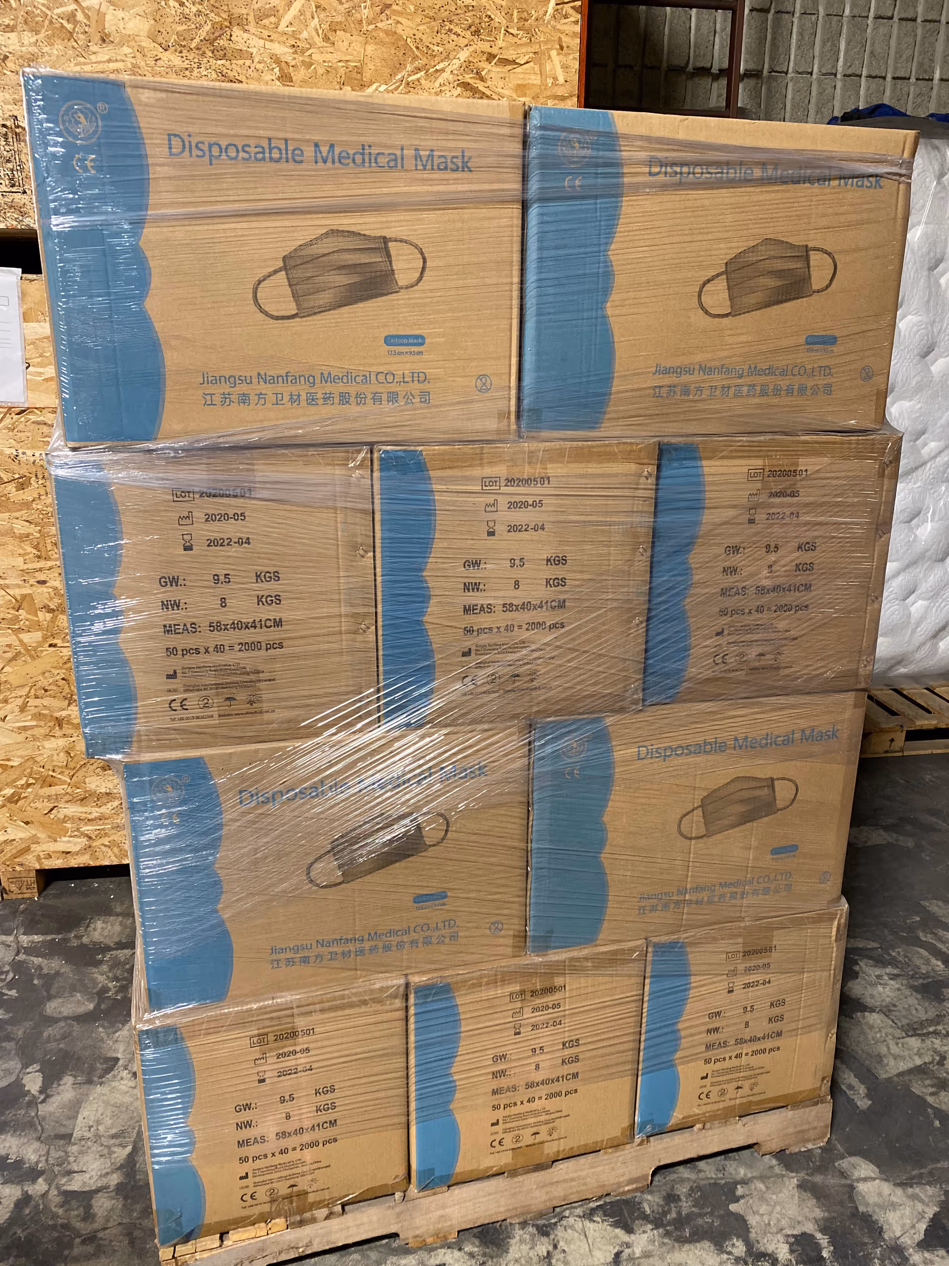 Stacks of disposable medical mask boxes on a pallet inside a storage area.