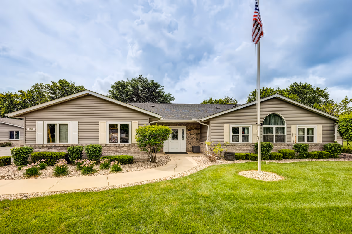 Single-story building with a manicured lawn, shrubs, and a flagpole in front.
