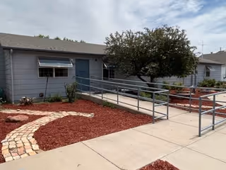 Exterior view of Florence Care Home showing a ramp, walkway, mulch beds, and a tree.