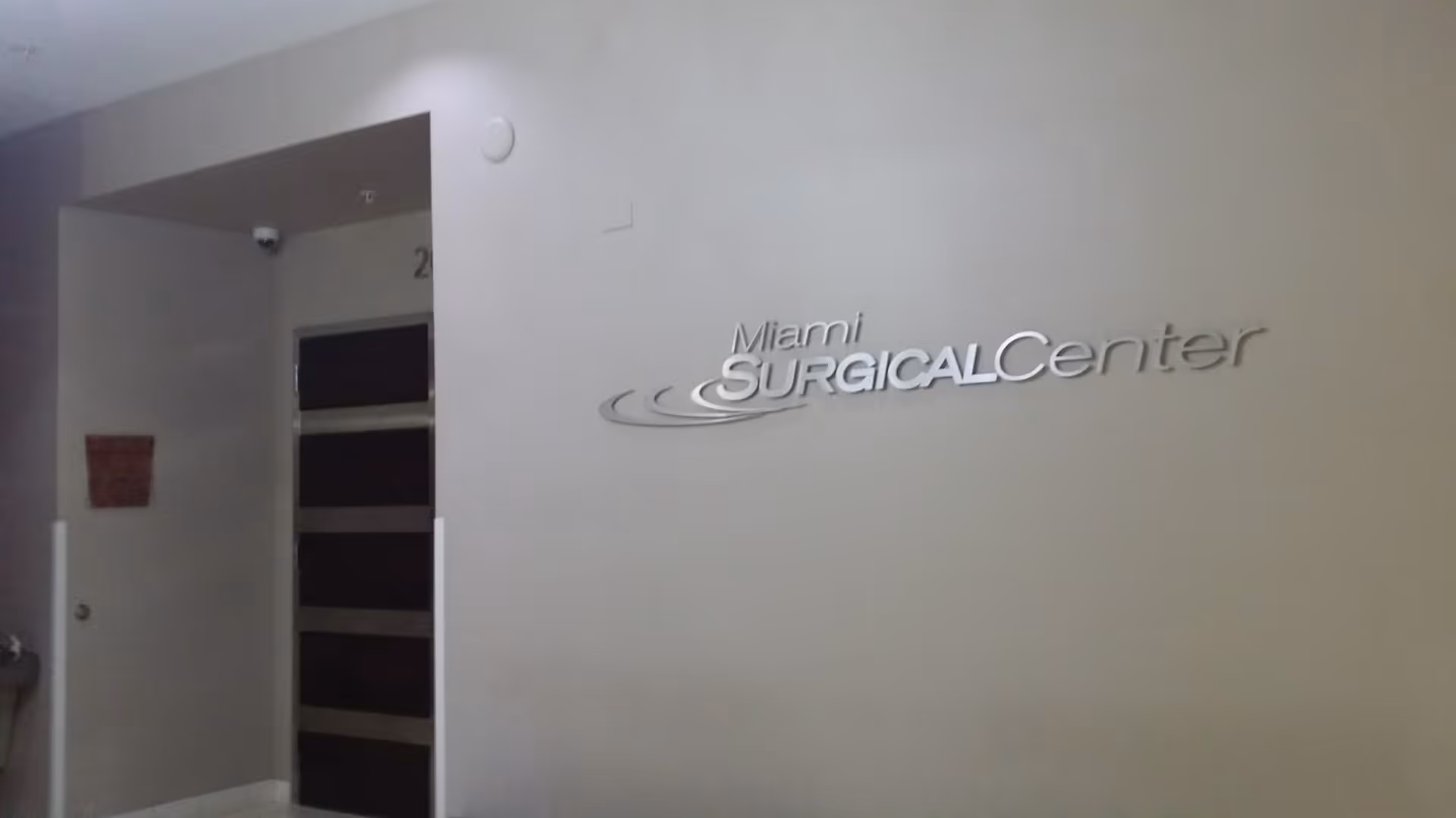 Interior hallway featuring Miami Surgical Center sign on light gray wall near doorway.