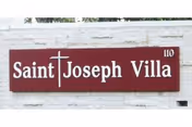 A red Saint Joseph Villa sign mounted on a white brick wall.