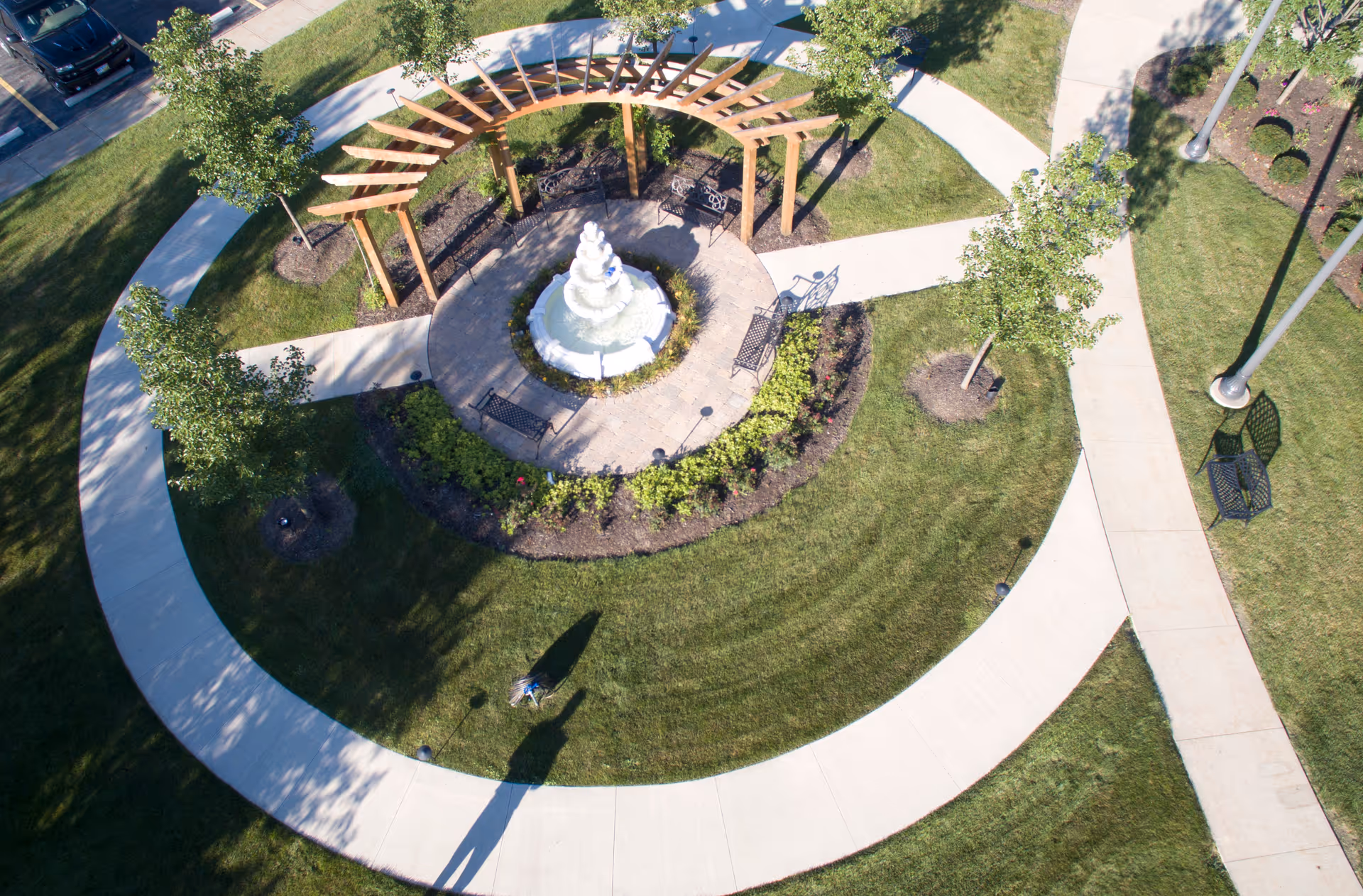 Aerial view of circular courtyard featuring a fountain, wooden arch structure, benches, and curved paths.