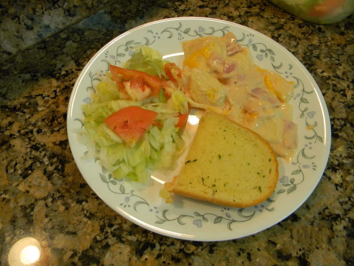 Plate with salad, potato casserole, and garlic bread on a granite kitchen counter.