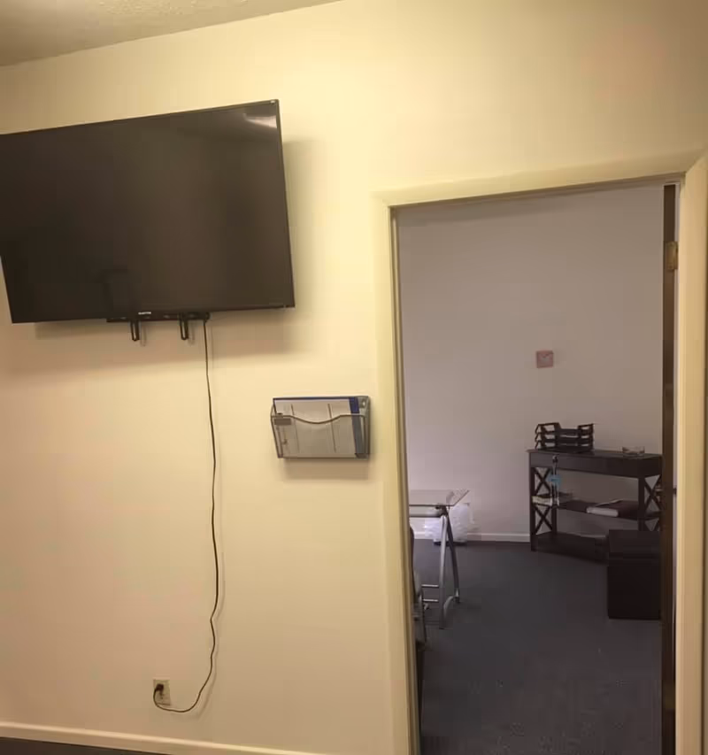 Interior wall with mounted flat-screen TV and doorway to a small staff area