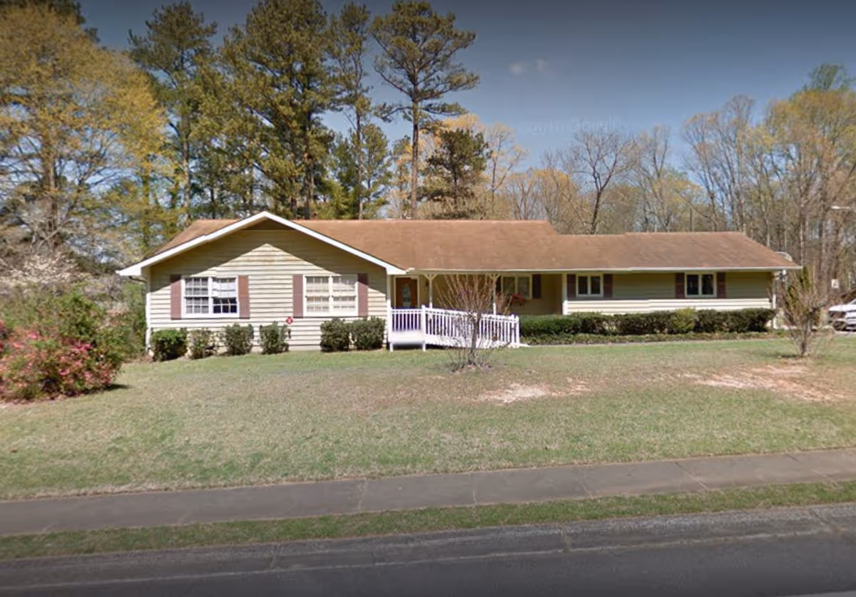 Single-story beige house with a small front porch and neatly trimmed shrubs.